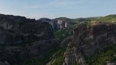 Meteora kaya oluşumlarının üzerinde süzülen hava manzaraları, yüksek uçurumlar ve canlı yeşillikler arasında yuva yapmış bir manastırı gösteriyor..