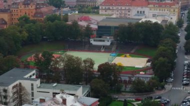 Havadan bakıldığında, Brno 'da futbol ve voleybol sahalarının yer aldığı canlı bir şehir manzarası görülüyor. Ağaçlar ve modern mimari ile çevrili park edilmiş arabalar caddelerde kuyruk oluşturuyor..
