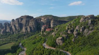 Yunanistan 'ın Meteora kentinde, Varlaam Manastırı' nın kayalık bir yüzeye tehlikeli bir şekilde tünediğini gösteren kameralar görülüyor. Arabalar aşağıdaki dolambaçlı yolda gidiyor..