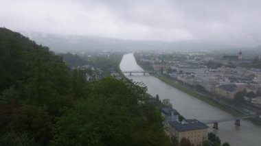 Salzach nehri bulutlu bir günde Salzburg şehir merkezinde dolanıyor. Yeşiller yemyeşil tepeler ve tarihi binalar resim gibi bir manzara yaratır..