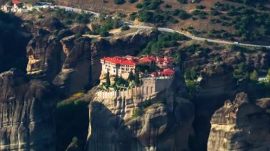 Yunanistan 'ın Meteora kentinde yükselen bir kaya oluşumunun tepesine tünemiş bir manastırın hava görüntüsü, güneş doğada gölgeler oluştururken.