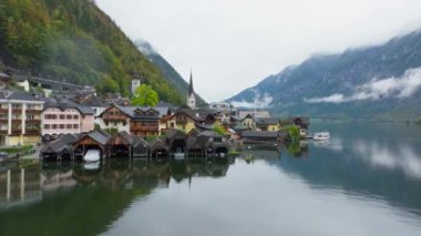 Tranquil Hallstatt, Avusturya 'da arka planda canlı evler, bir kilise kulesi ve görkemli Alpler sergileniyor. Tekneler turistleri sakin gölün karşısına geçirir..