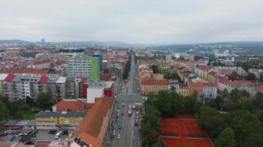 Hava görüntüleri Brno şehir merkezini yakalıyor, bulutlu bir günde binalar arasında yoğun bir yolda hareket eden arabalar ve tramvaylar sergileniyor, kentsel yaşam ve ulaşım dinamiklerini vurguluyor.