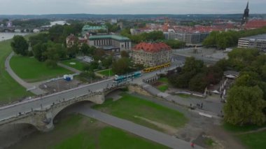 Dresden, Almanya 'da Augustus Köprüsü' nden geçen sarı bir tramvay görüntüsü var. Yayalar ve araçlar kalabalık bir şehir manzarası yaratıyor..