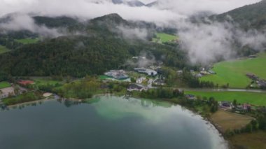 Fuschlsee Gölü 'nün üzerinde hareket eden bulutların havadan görünüşü, arka planda Alpler dağlarıyla birlikte kıyıdaki Kızıl Boğa Karargahını ortaya çıkarıyor..