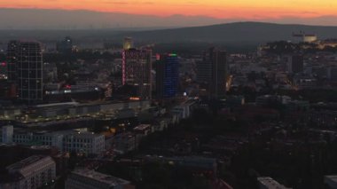 Gün batımında Bratislavas 'ın gökyüzü manzarası. Şehir ışıkları yavaş yavaş modern gökdelenleri aydınlatıyor. Güneş dağların ardında batıyor..