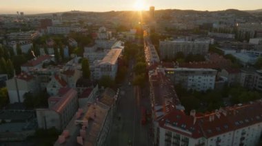 Bratislava, Slovakya 'da bir caddeyi aydınlatan gün batımı, sıcak bir parıltıyla apartman ve şehir binalarını yıkıyor, akşam manzarasının cazibesini vurguluyor..