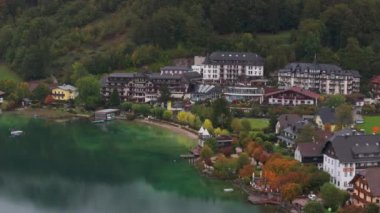 Avusturya Alpleri 'ndeki Fuschlsee Gölü kıyısında lüks bir tatil köyünü gösteren kamera. Renkli binalar ve sonbahar yaprakları gölün yeşil sularını sarar..