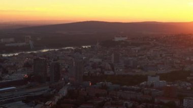 Slovakya, Bratislava 'nın altın bir günbatımının altında parlayan yüksek açılı üç ayaklı görüntüsü. Tarihi ve modern mimarinin eşsiz bir perspektiften uyum içinde harmanlandığı çarpıcı şehir manzarası..