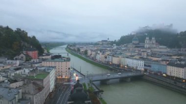 Salzburg tarihi merkezinin içinden Salzach Nehri akan ve arkasında Hohensalzburg Kalesi olan eşsiz bir noktasından üç ayaklı manzara. Alçak bulutlar sabah yavaş yavaş eriyor..
