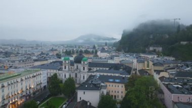 Yüksek açılı tripod manzarası, Salzburg, Avusturya 'nın sislerin yavaş yavaş kalktığını, tarihi binalar, büyüleyici çatılar ve Kutsal Üçlü Kilise ile dolu çarpıcı bir şehir manzarasını gözler önüne seriyor..