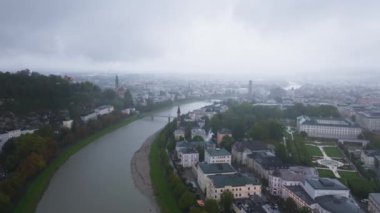 Hava görüntülerinde Salzburg, Avusturya, Salzach Nehri bulutlu bir günde şehir merkezinde kıvrılarak tarihi mimari ve doğal güzelliğin karışımını vurguluyor..