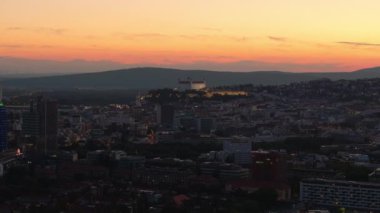 Bratislavas silueti gün batımında parlayarak bir tepenin üstündeki kaleyi aydınlatır. Canlı renkler ve sakin bir atmosfer büyüleyici akşam sahnesini tanımlar..