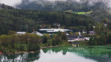 Avusturya Alpleri 'ndeki bir gölün yakınındaki Kızıl Boğa karargahının hava manzarası. Binalar ve ağaçlar göle yansıyor..