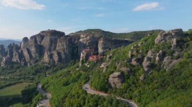 Yunanistan 'ın Meteora kentinde, Varlaam Manastırı' nın kayalık bir yüzeye tehlikeli bir şekilde tünediğini gösteren kameralar görülüyor. Arabalar aşağıdaki dolambaçlı yolda gidiyor..