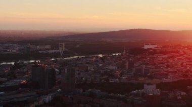 Güneş Bratislava, Slovakya 'da batıyor. Şehir binaları, Tuna Nehri ve uzak UFO Köprüsü' nün üzerine turuncu bir parıltı saçıyor..