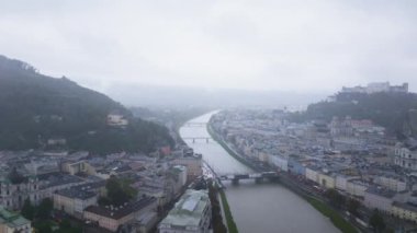 Kamera Avusturya 'nın Salzburg şehrinde ilerliyor. Salzach Nehri şehir merkezine doğru akıyor. Sağda Hohensalzburg Kalesi var..