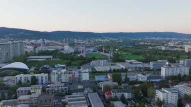 Hava görüntülerinde Bratislava, Slovakya, Ulusal Futbol Stadyumu, Tehelne Pole, nefes kesici bir gün batımına karşı, şehirlerin canlı ufuk çizgisini ve ufuk çizgisini vurguluyor..