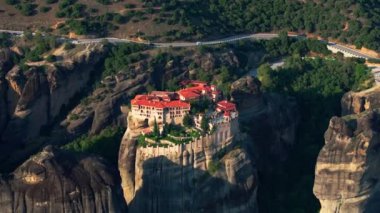 Sıcak güneş ışığı dramatik bir kaya oluşumunun üzerinde bir manastırı yıkıyor Yunanistan 'ın Meteora kentinin çarpıcı mimarisi ve doğal güzelliğini vurguluyor.