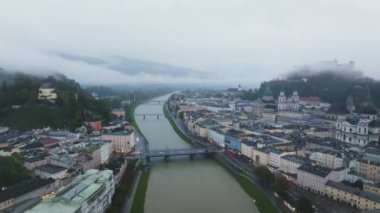 Salzburg, Avusturya 'nın hava manzarasında Salzach Nehri, Hohensalzburg Kalesi ve şehir manzarası yer almaktadır. Alçak bulutlar şehrin üzerinden geçiyor..