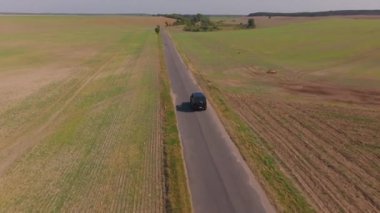 Yeşil tarlaların arasından geçen siyah bir SUV 'un hava görüntüsü. Araba yavaş hareket ediyor ve manzaranın tadını çıkarıyor..