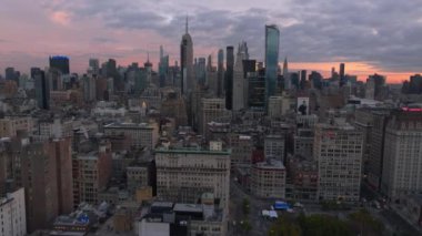 Gökdelenler New York 'un alçak binaları üzerinde kule gibi yükselirken, parlak pembe ve mor bulutlar gün batımında gökyüzünü dolduruyor..