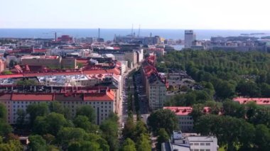 Helsinki, Finlandiya 'da geleneksel binalar, yemyeşil bir park ve arka planda Baltık Denizi bulunan bir caddenin havadan görünüşü.