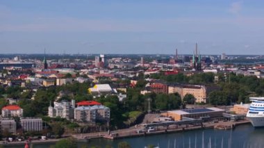 Helsinki, Finlandiya 'nın hava manzarası, Uspenski Katedrali ve canlı bir limanın yer aldığı şehrin ufuk çizgisinin, tüylü bulutlarla kaplı parlak mavi bir gökyüzüne karşı kurulduğunu gösteriyor..