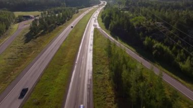 Finlandiya 'nın başkenti Helsinki' ye giden otoyolda, yemyeşil ormanların çerçevelediği hava manzaralı araçlar ön plana çıkıyor. Sahne, yaz manzarasını ve kentsel gelişimi yakalıyor..