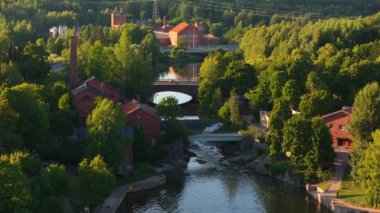 Helsinki, Finlandiya 'da köprüden geçen beyaz bir arabanın hava görüntüsü. Yeşiller yemyeşil ağaçlar ve kırmızı tuğlalar nehir kıyısında..