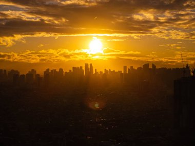 Glowing sunset casting stunning silhouette of Manila city skyline against golden clouds, showcasing the urban landscape. clipart