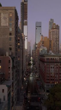 Dikey videolarda, New York 'ta, Manhattan' daki Beşinci Cadde 'de hava kararırken gökdelenlerle çevrili araçlar görülüyor..