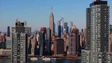 Queens 'ten Doğu Nehri' ne yayılan kamera Manhattan şehir merkezinin siluetini gözler önüne seriyor. Empire State Binası gökdelenlerin arasında dikiliyor..