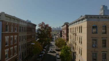 Williamsburg, Brooklyn 'de renkli sonbahar ağaçlarıyla kaplı bir caddenin üzerinde kameralar var. Manhattan silueti uzaktan görülebiliyor.