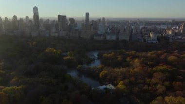 Sıcak sabah ışığı Central Park 'ı ve Manhattan şehir merkezini sarar, binalardan ve sonbahar ağaçlarından gölgeler bırakır, New York' un sakin şehir atmosferini.