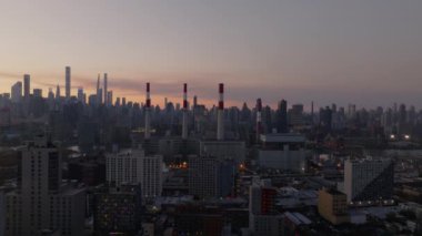 Batan güneş New York şehrinin ikonik silueti üzerinde turuncu bir parıltı saçıyor. Queens ve East River 'daki Ravenswood endüstriyel bacalarını vurguluyor..