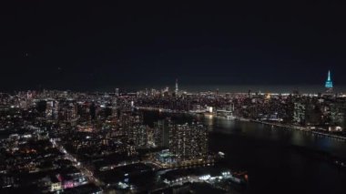 Doğu Nehri 'nin manzarası New York Citys' in gece aydınlanmış gökyüzünü gösteriyor. Canlı ışıklar ve Manhattan 'ın kentsel manzarasını tanımlayan ikonik gökdelenler sergiliyor..