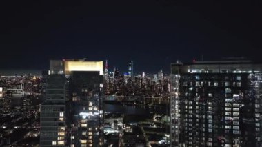 Aydınlatılmış New York şehri gökyüzü geceleri büyülüyor, East River canlı şehir ışıklarını yansıtıyor. Gökdelenler ve simgeler çarpıcı şehir manzaraları yaratıyor..