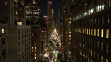 Geceleri New York 'ta Manhattan' da kalabalık bir caddede arabalar sürüyor. Apartman pencereleri aydınlandı, yayalar yürüyor ve erkekler dışarıda çalışıyor..