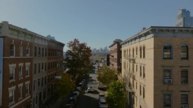 Williamsburg, Brooklyn 'de renkli sonbahar ağaçlarıyla kaplı bir caddenin üzerinde kameralar var. Manhattan silueti uzaktan görülebiliyor.