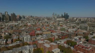 Brooklyn 'deki Williamsburg mahallesinde hava görüntüsü var. Yoğun binaların üzerinde kayan kamera, arka plandaki uzak Manhattan siluetini ortaya çıkarıyor..