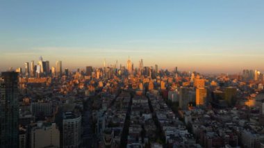 New York 'u çevreleyen sıcak güneş ışığının kuşbakışı manzarası Manhattan şehir merkezindeki binalar, altın saat boyunca gökyüzünü canlı renklerle boyuyor..
