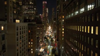 Geceleri New York 'ta Manhattan' da kalabalık bir caddede arabalar sürüyor. Apartman pencereleri aydınlandı, yayalar yürüyor ve erkekler dışarıda çalışıyor..