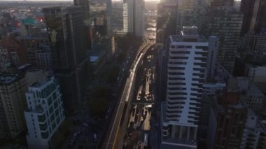 Günbatımı ışınları yükselen metro treni Queens 'in siluetinde süzülüyor mimari manzaraya karşı dramatik gölgeler yaratıyor..