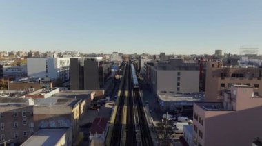 Metropolitan metro treni yükseltilmiş raylarda süzülüyor, güneşli şehir manzarasını dilimliyor, Queens, New York 'ta kentsel ulaşım enerjisini ve hareketini yakalıyor..