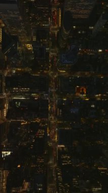 Aydınlatılmış Manhattan sokakları gece yavaş çekimde canlanıyor, canlı ışıklar, yoğun trafik, ikonik New York gökdelenleri taşınabilir dost formatında resmedilmiş.