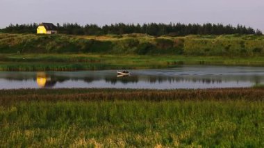 Balıkçı teknesini Danimarka 'daki bir nehrin sakin sularına götürür. Güneş batar ve yeryüzüne sıcak bir ışıltı saçar..