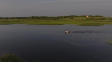 Ringkobing Fjord 'un sakin sularında, sakin kıyı şeridini noktalayan uzak bir evle motorlu bir teknede yüzen bir balıkçıyı görüntüler..