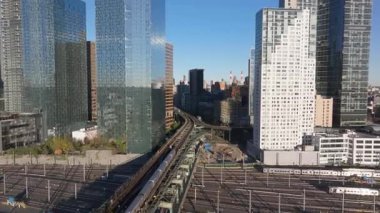 Metro treni, yükseltilmiş raylar, New York silueti ışıldıyor, güneş ışığı şehir ulaşımı altyapısını havadan aydınlatıyor..