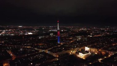 Gece Prag silueti üzerinde parlayan Zizkov Televizyon Kulesi, göz kamaştırıcı şehir ışıklarının altında, önplandaki Ulusal Anıtı vurguluyor.